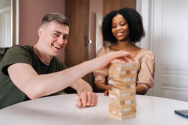 De joyeux amis multiethniques passent du temps ensemble à jouer dans une tour en bois de crash de jeu de société à la maison Heureux groupe diversifié s'amusant ensemble