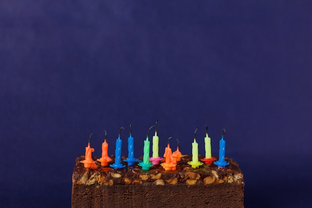 Joyeux anniversaire Brownie Cake avec des arachides, du caramel salé et des bougies colorées non éclairées sur le fond violet. Copiez l'espace pour le texte.