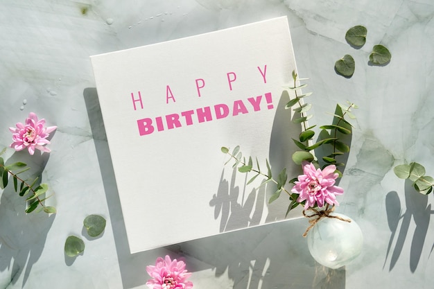 Joyeux anniversaire texte sur toile carrée et hiver, décorations du début du printemps. Fleurs de chrysanthème rose, eucalyptus dans un vase en verre sur pierre vert menthe. Conception de carte de voeux dans des couleurs pastel à la mode.