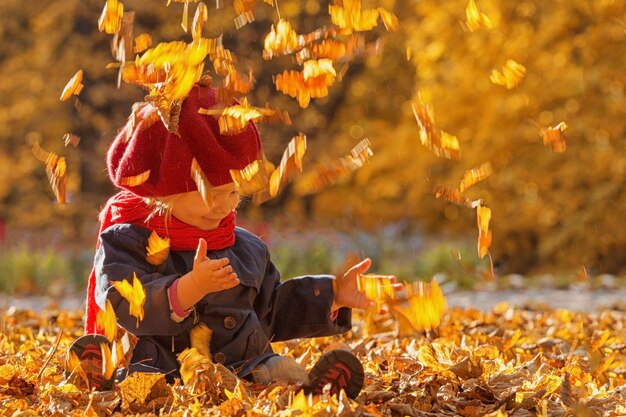 Joyeux automne Une petite fille dans un béret rouge joue avec les feuilles qui tombent et rit