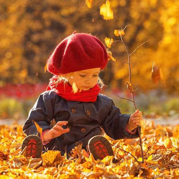 Joyeux automne Une petite fille dans un béret rouge joue avec les feuilles qui tombent et rit