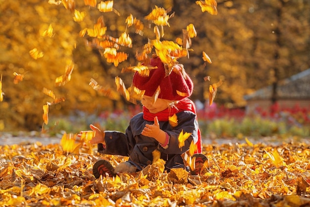 Joyeux automne Une petite fille dans un béret rouge joue avec les feuilles qui tombent et rit