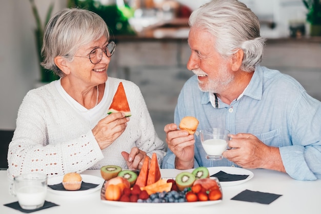 Joyeux beau couple de personnes âgées à la maison prenant son petit déjeuner avec du lait muffin et des fruits frais de saison concept de saine alimentation