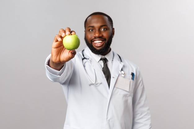 Joyeux beau docteur afro-américain donnant patient pomme verte, montrant des fruits demander manger des fruits et des vitamines