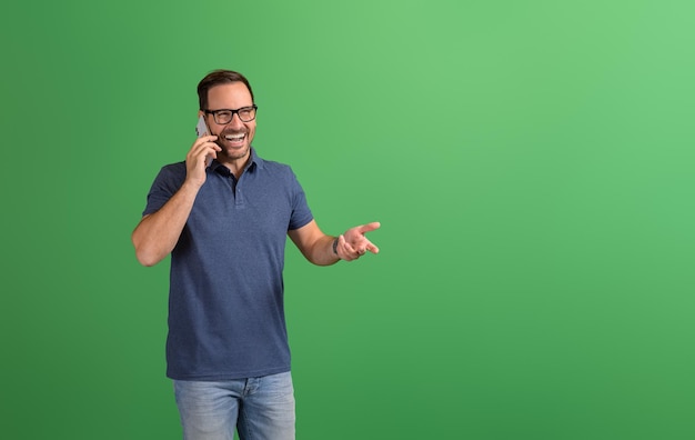 Un joyeux et beau freelance discutant sur son téléphone portable et détournant le regard sur un fond vert.