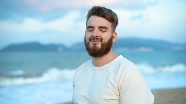 Photo joyeux beau gars libre jeune calme détendu homme insouciant voyageur profiter de la mer sur la plage vue sur l'océan