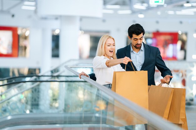 Joyeux beau jeune couple souriant parlant tenant des sacs en papier avec des achats dans un centre commercial