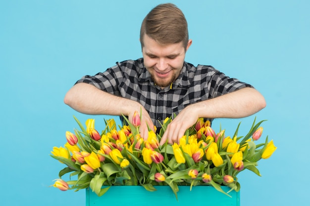 Joyeux bel homme fleuriste tenant boîte de tulipes sur mur bleu,