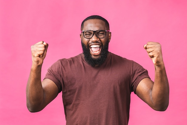 Joyeux bel homme noir afro-américain faisant un geste oui tout en étant excité de gagner. Un jeune fan extatique s'enracine et exprime son soutien. Concept de réussite isolé sur fond rose.