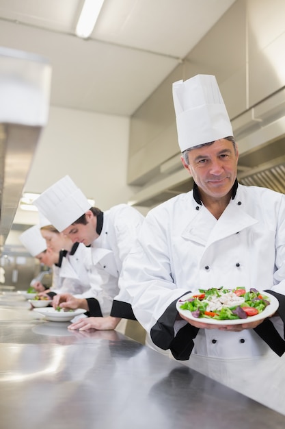 Joyeux chef montrant sa salade avec des travailleurs en arrière-plan