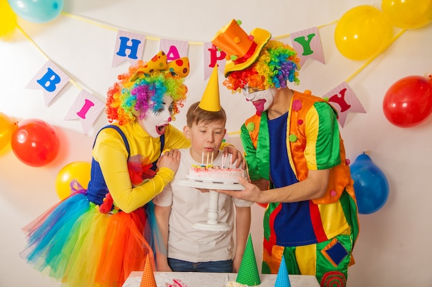 Joyeux clowns émotionnels lors de vacances avec des enfants soufflent le gâteau