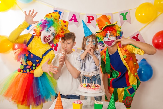 Joyeux clowns émotionnels lors de vacances avec des enfants soufflent le gâteau