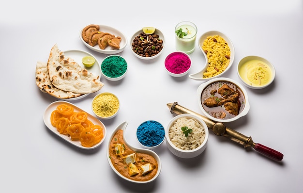 Joyeux concept sacré montrant un assortiment de plats indiens pour le déjeuner comme du poulet paneer beurre masala naan jeera riz noir chana fry jalebi ras malai thandai et farsan avec des couleurs holi et pichkari