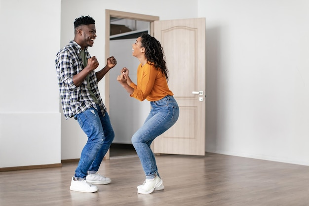 Joyeux couple africain secouant les poings célébrant le déménagement dans une nouvelle maison