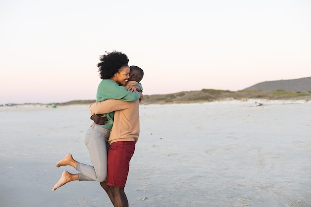 Joyeux couple afro-américain embrassant et souriant sur la plage au coucher du soleil, espace de copie. L'été, la convivialité, la romance et les vacances, inchangés.