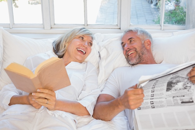 Joyeux couple d&#39;âge mûr avec journal et livre au lit