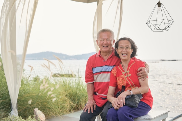 Joyeux couple asiatique âgé se reposant au bord de la mer par une journée ensoleillée, concept de bonne retraite, voyage pour le concept de vacances du Nouvel An lunaire chinois