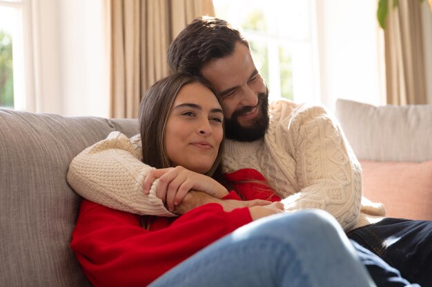 Photo joyeux couple caucasien assis sur un canapé dans le salon, souriant et embrassant. concept de vie domestique, de loisirs, de romance et de convivialité.