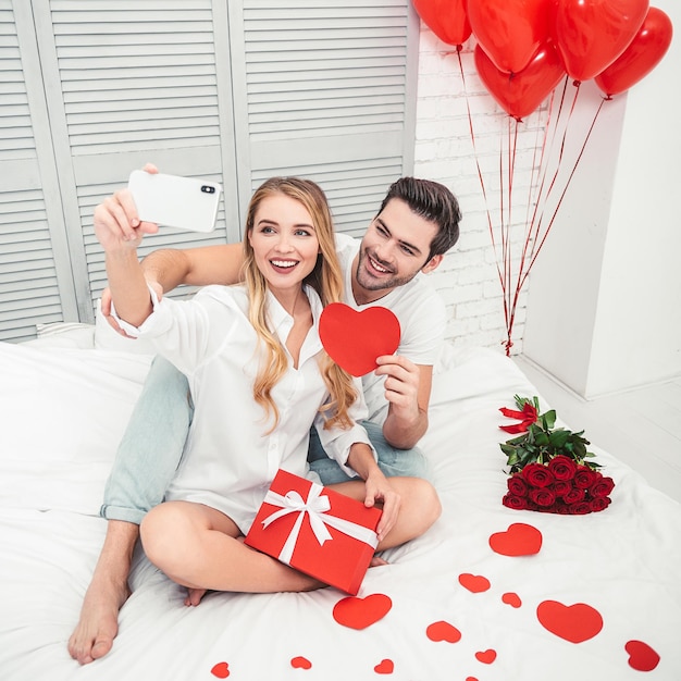 Joyeux couple caucasien prenant selfie sur smartphone assis sur le lit concept de la saint-valentin