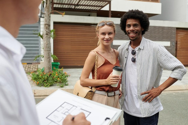 Joyeux couple discutant du plan de la maison qu'ils vont regarder avec l'agent immobilier