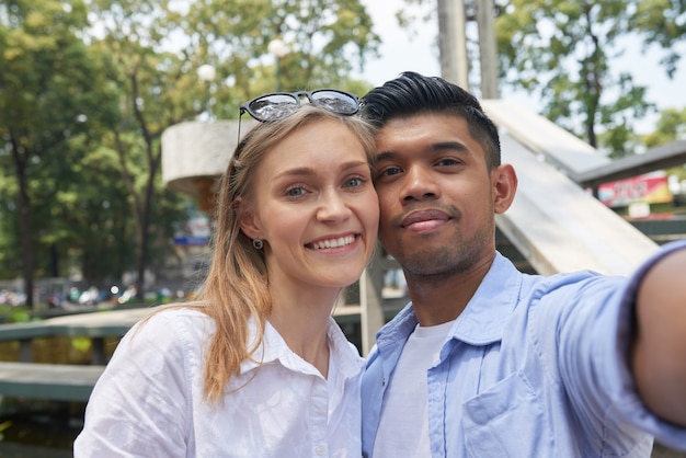 Joyeux couple diversifié souriant prenant un selfie sur un smartphone en marchant dans la ville où ils se sont rendus