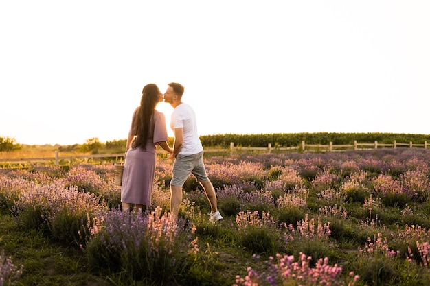 Joyeux couple élégant debout au champ de lavande souriant ayant un rendez-vous romantique au coucher du soleil