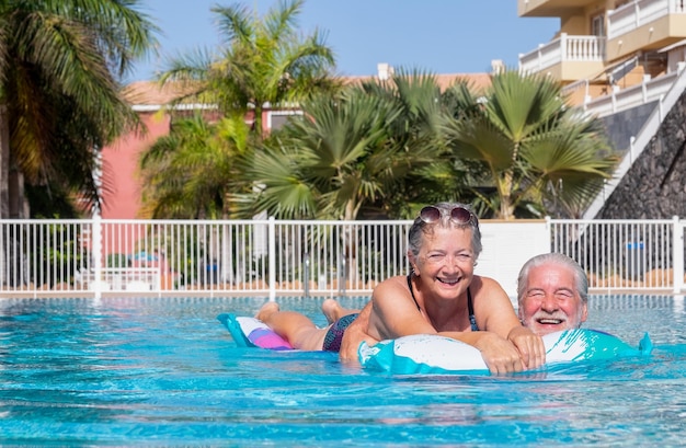 Joyeux couple de grands-parents souriant dans la piscine flottant sur un matelas