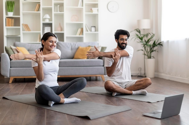 Joyeux couple indien pratiquant le yoga à la maison qui s'étend sur un tapis de fitness