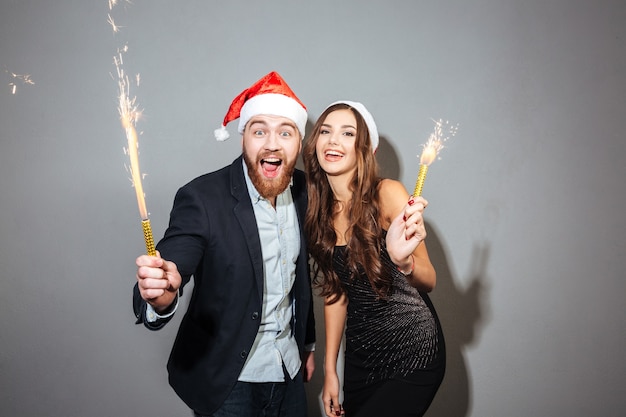 Joyeux couple joyeux célébrant tenant des verres avec du champagne et des pétards sur un mur gris