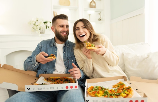 Joyeux couple mangeant de la pizza devant la télé