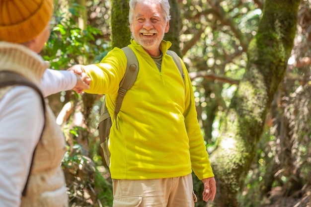 Joyeux couple senior caucasien en randonnée dans la forêt tenant des sacs à dos et se regardant la main dans la main