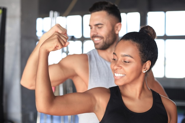 Joyeux couple sportif s'entraînant ensemble et montrant des biceps au gymnase.