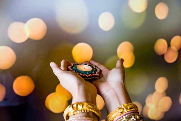 Joyeux Diwali - Mains de femme au henné tenant une bougie allumée isolée sur fond sombre. Lampes en argile Diya allumées pendant Dipavali, fête hindoue des lumières. Copiez l'espace pour le texte.