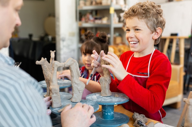 Joyeux élève souriant largement tout en modelant des figures d'argile