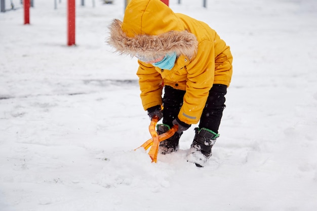 Joyeux enfant adorable avec fabricant de boules de neige s'amusant dans la neige dans la ville Plaisirs d'hiver à l'extérieur Concept de vacances d'hiver