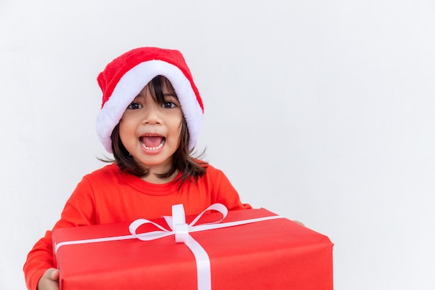 Joyeux enfant asiatique au chapeau rouge de Santa tenant des cadeaux de Noël. Temps de Noël.sur fond blanc.