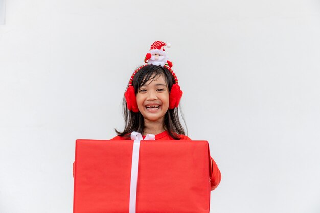 Joyeux enfant asiatique au chapeau rouge de Santa tenant des cadeaux de Noël. Temps de Noël.sur fond blanc.