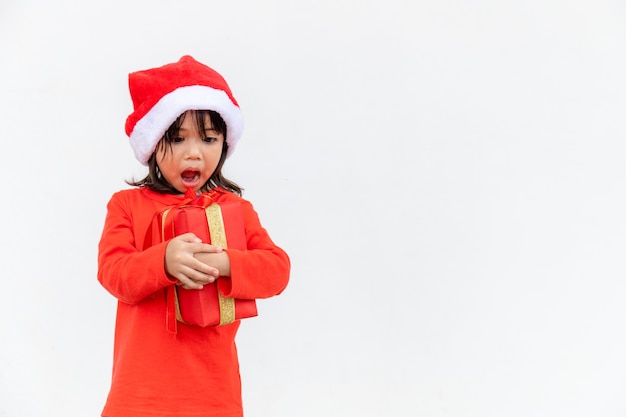 Joyeux enfant asiatique au chapeau rouge de Santa tenant des cadeaux de Noël. Temps de Noël.sur fond blanc.