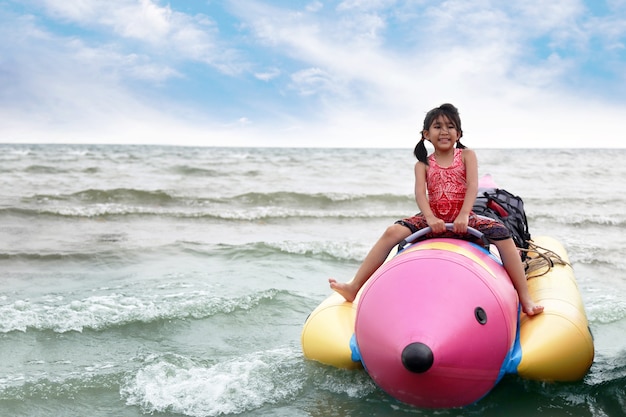 Joyeux enfant asiatique sur un bateau en plastique sur la plage en été