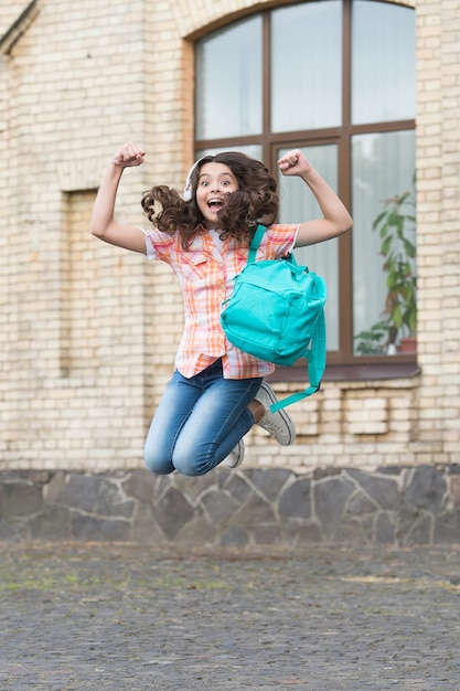 Joyeux enfant énergique qui saute avec un sac d'école dans un style décontracté dans la cour d'école, les vacances.