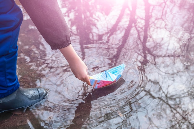 Joyeux enfant garçon de 67 ans dans des bottes en caoutchouc jouant avec des bateaux en papier origami dans une flaque de boue temps heureux de l'enfance insouciante