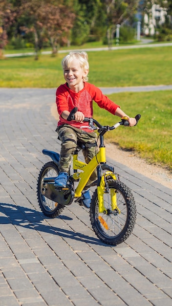 Joyeux enfant garçon d'années s'amusant dans le parc avec un vélo au format vertical de belle journée pour