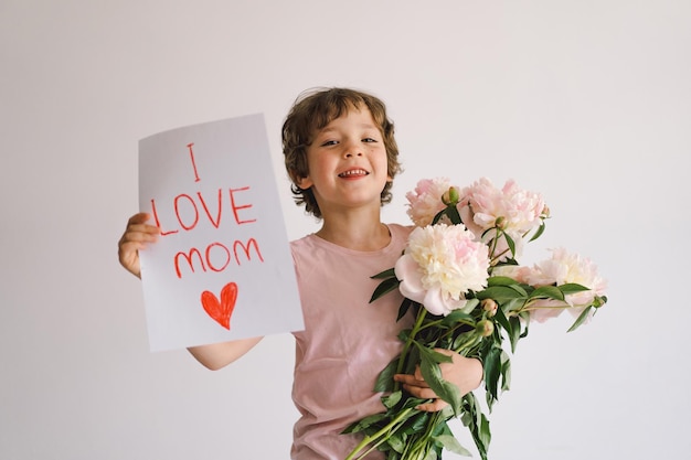 Joyeux enfant heureux avec bouquet de pivoines Petit garçon souriant sur fond blanc Concept de la fête des mères