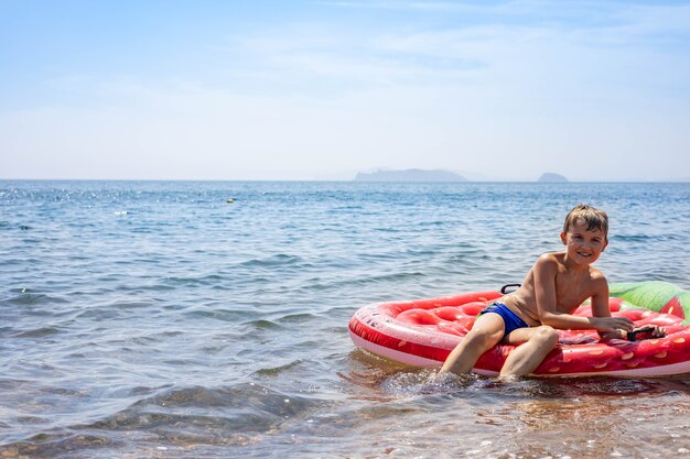 Joyeux enfant mâle jouant flottant sur une bouée de sauvetage gonflable en caoutchouc entourée d'eau de mer