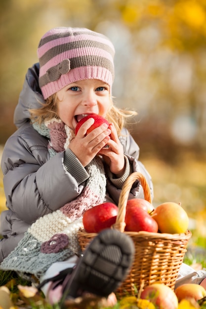 Joyeux enfant mangeant une pomme rouge dans un parc en automne. Concept de modes de vie sains