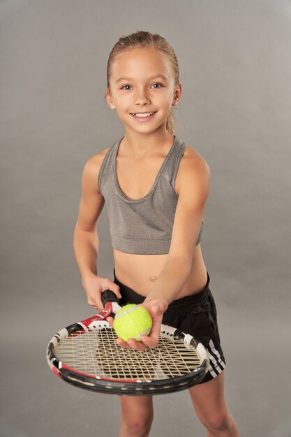 Joyeux enfant de sexe féminin tenant une raquette de tennis et une balle