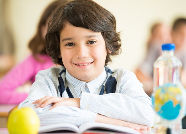 Joyeux enfants assis avec apple et globe sur le bureau dans la salle de classe