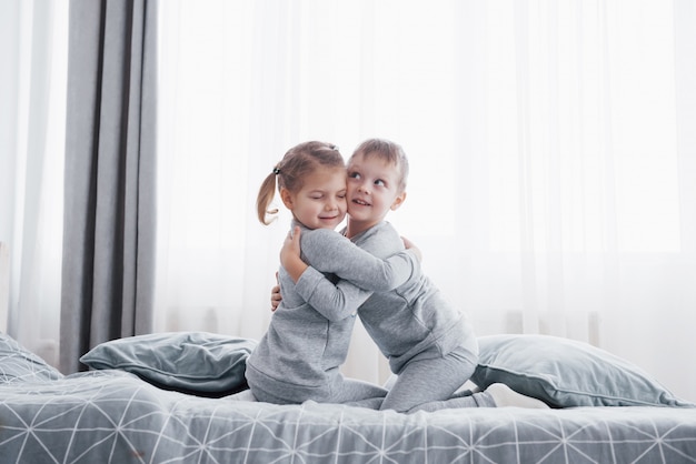 Joyeux enfants jouant dans la chambre blanche. Petit garçon et fille, frère et soeur jouent sur le lit en pyjama.