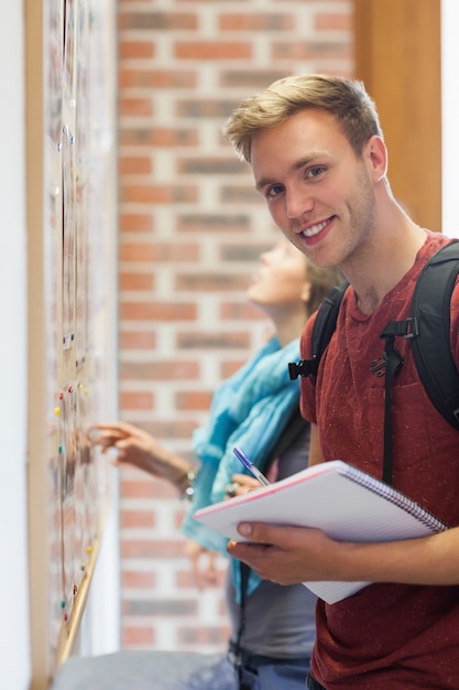 Joyeux étudiant à la recherche de quelque chose sur le tableau d&#39;affichage