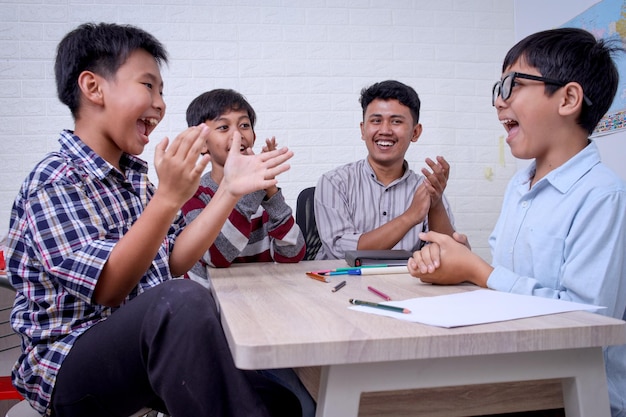 De joyeux étudiants asiatiques et un enseignant applaudissent sur un bureau d'école en classe